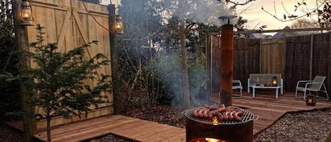 Takapihalla on puilla lämmitettävä grilli, puinen terassi ja oleskelualue, jossa on tuoleja.