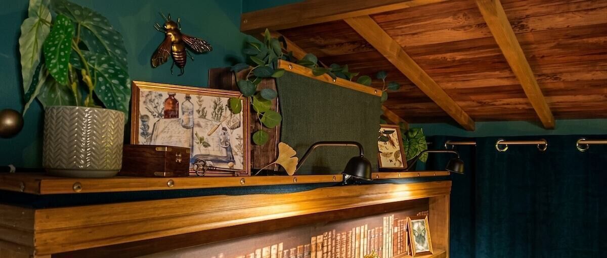 Une étagère en bois ornée d’un pot de fleurs, de quelques photos encadrées et d’une petite lampe.