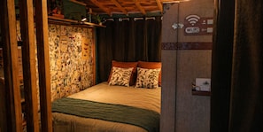 A bedroom with a bed, pillows, a blanket, a wall with various pictures, a Wi-Fi sign, and a door with a lock. - Tiny house perdue  logement insolite Baie de Somme (Saint Blimont)