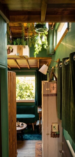 Une pièce chaleureuse avec un plafond en bois, un mur vert, une fenêtre donnant sur un beau paysage, un banc, une table avec une horloge et un piano.