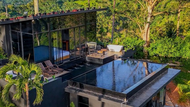 A modern glass house with a rooftop pool, outdoor seating, and lush greenery. - Charming 1-bedroom with Ocean View - A God's View (Las Palmillas)