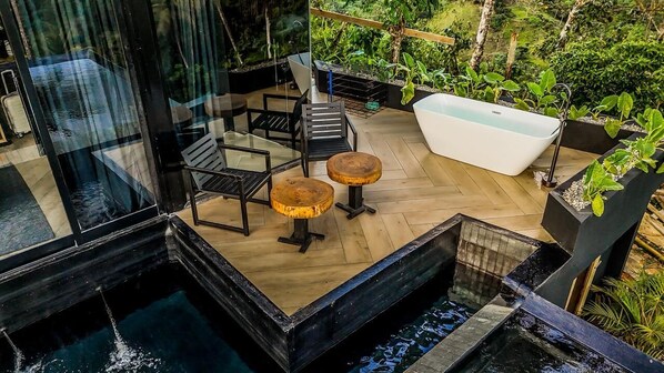 A modern outdoor terrace with a glass enclosure, wooden flooring, a white bathtub, and surrounding greenery. - Charming 1-bedroom with Ocean View - A God's View (Las Palmillas)