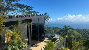 A modern building with a glass facade, outdoor seating, and a view of the ocean. - Charming 1-bedroom with Ocean View - A God's View (Las Palmillas)