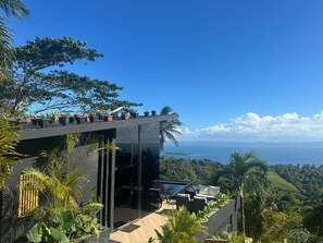 A modern building with a glass facade, outdoor seating, and a view of the ocean. - Charming 1-bedroom with Ocean View - A God's View (Las Palmillas)