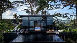 A modern glass house with a bed, outdoor seating, and a pool. - Charming 1-bedroom with Ocean View - A God's View (Las Palmillas)