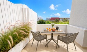 A balcony with a table set for breakfast, two chairs, and a view of buildings in the distance. - Art Apartment | 80m from the Beach with Balcony & Private Parking (Palaiochora)