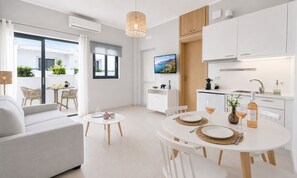 Ein modernes Wohnzimmer mit einer Couch, einem Esstisch für zwei Personen und einer Küchenzeile mit weißen Schränken sowie einem Fernseher.