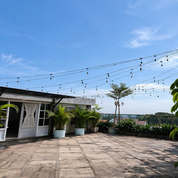 A rooftop terrace with potted plants, string lights, and a view of the landscape. - Hot In Hotel (Depok)