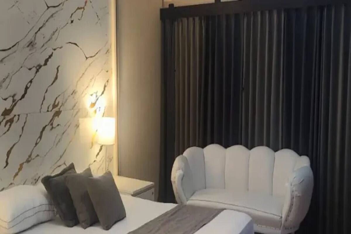 Et hotelværelse med en seng, en hvid polstret stol, væg med marmorering og en mørk gardin.