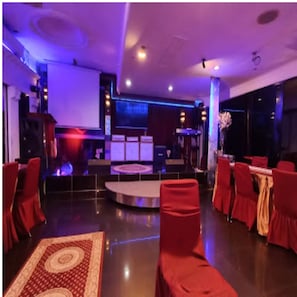 A spacious room with a stage, red chairs, and tables arranged for an event.