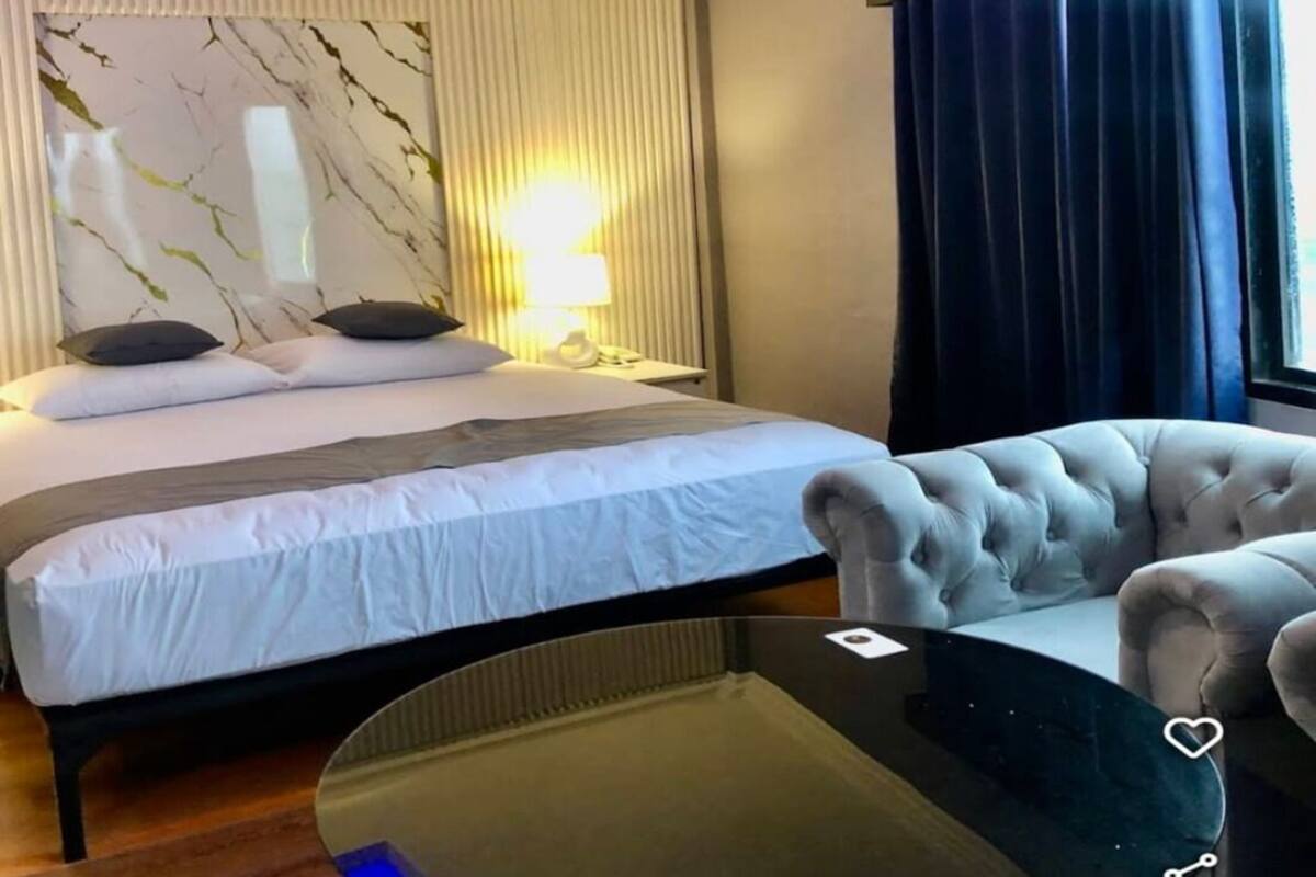 Et hotelværelse med en seng, et natbord med en lampe, en stol og udsigt til det fri gennem et vindue.