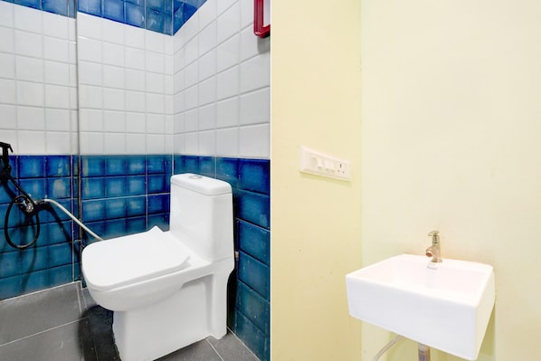 A bathroom with a toilet, a sink, and a shower area. - Deluxe Shree Srinivasa Hotel (Hyderabad)