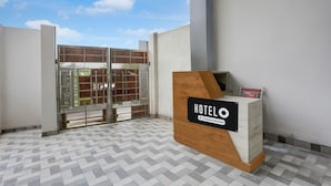 A hotel reception desk with a sign, a tiled floor, and a glass door leading outside. - Super Deluxe Room Mohini Guest House (Bareilly)