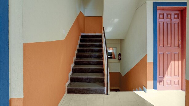 A staircase with a handrail, a fire extinguisher, and a red door. - Deluxecrystal Holiday Homes (Calangute)