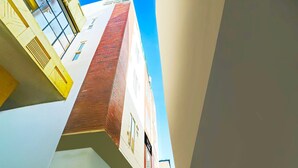 Um edifício com vários andares, fachada de tijolos vermelhos, paredes brancas e um céu azul claro.