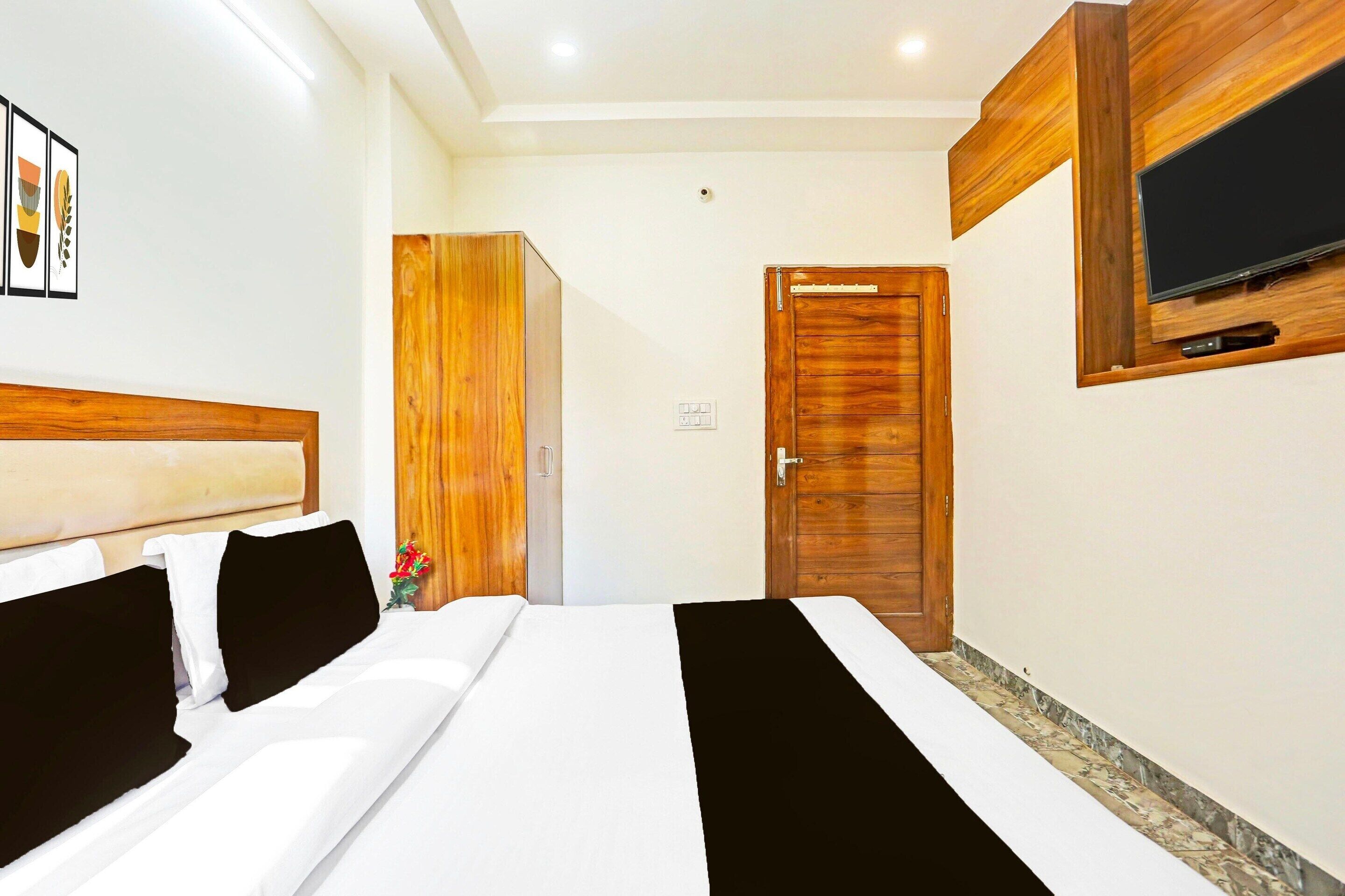 A hotel room with a bed, a wooden wardrobe, a television mounted on the wall, and a door.