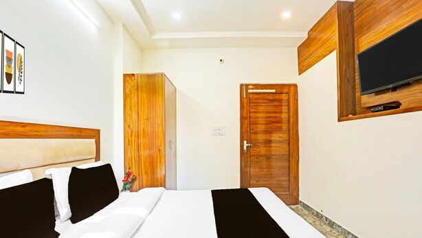 Quarto de hotel com cama, guarda-roupa de madeira, televisão na parede e uma porta.