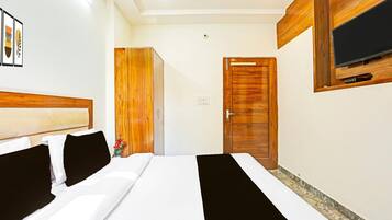 A hotel room with a bed, a wooden wardrobe, a television mounted on the wall, and a door.