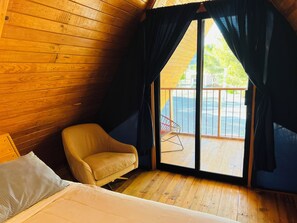 A room with wooden walls, a bed, a chair, and a sliding glass door to an outdoor area.