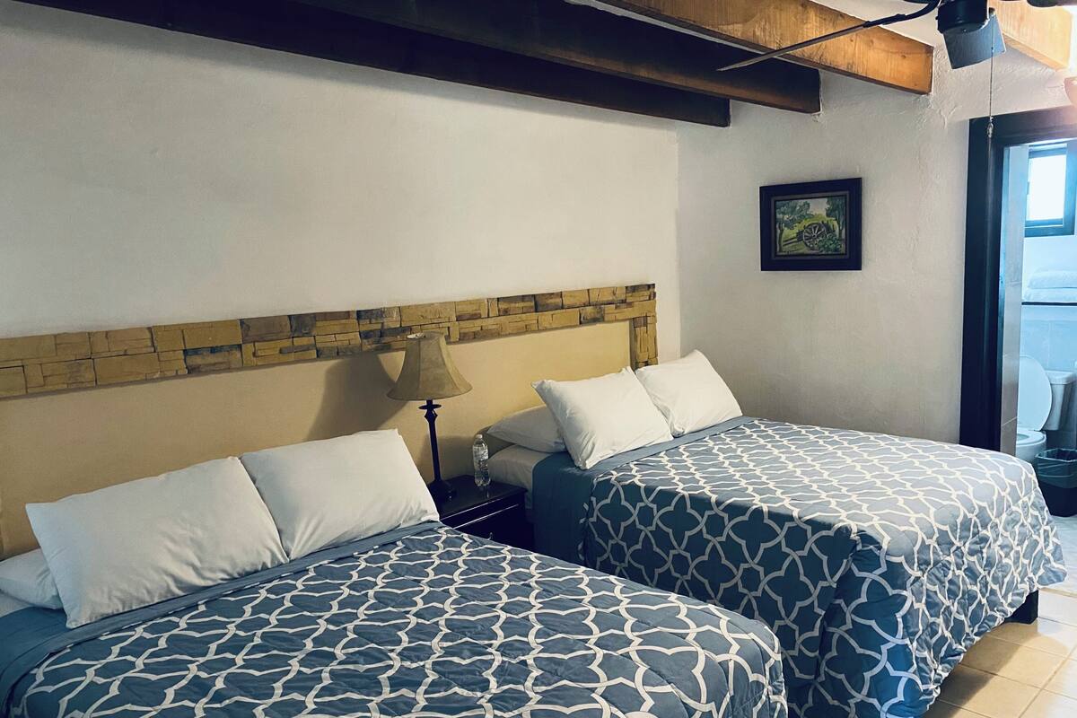 Dos camas con ropa de cama estampada, una mesita de noche con lámpara, una pared de acento de piedra y un cuadro en la pared.