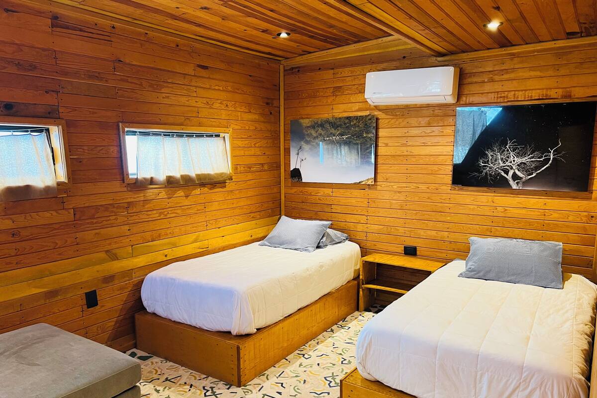 Una habitación tipo cabaña de madera con dos camas, un banco y un suelo estampado.