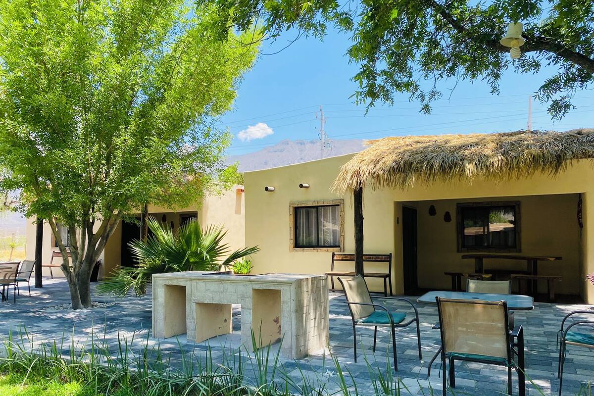Un patio con mobiliario exterior, una estructura de techo de paja y vistas a la montaña.