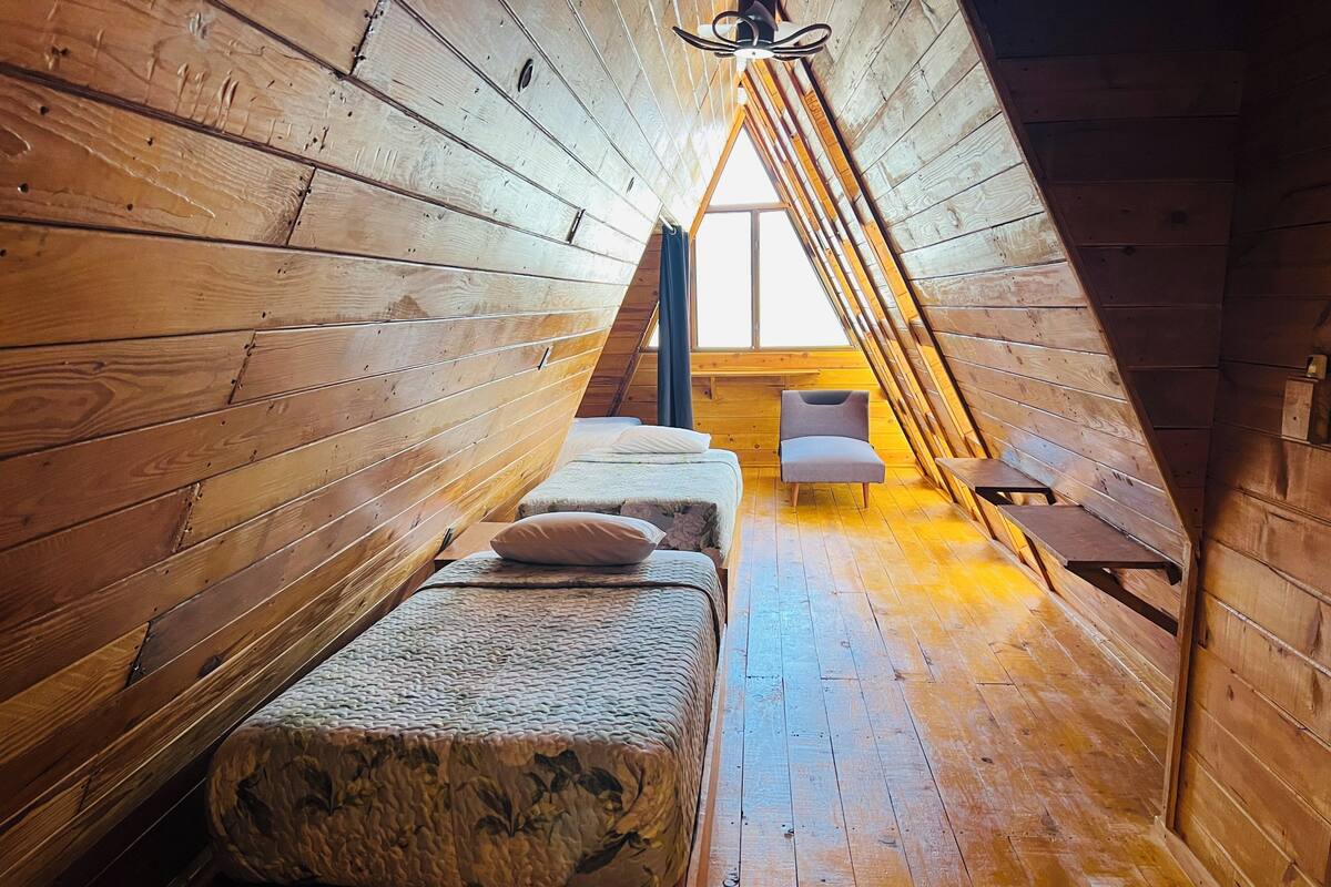Habitación con techo inclinado, paredes de madera, una cama, una silla y una mesita.