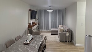 En moderne stue med spiseplads, en sofa, et tv ophængt på væggen og en loftlampe.