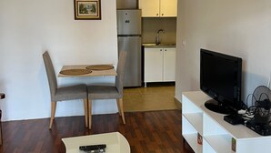 Kompakti oleskelutila, jossa on ruokapöytä, televisio, keittiöalue ja kattovalaisin.