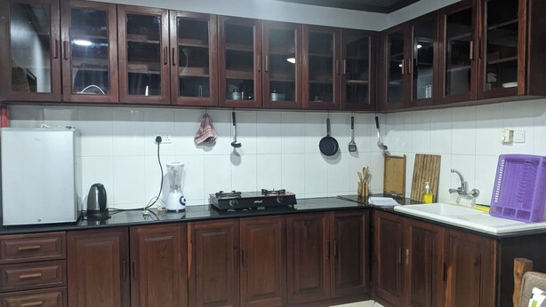 A kitchen with wooden cabinets, a refrigerator, a stove, and various utensils. - Kay's Place Cultural Apartment Zanzibar Gallery (Zanzibar)