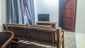 A room with a woven sofa, a small wooden table, a television, and a door. - Kay's Place Cultural Apartment Zanzibar Gallery (Zanzibar)