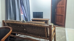A room with a woven sofa, a small wooden table, a television, and a door. - Kay's Place Cultural Apartment Zanzibar Gallery (Zanzibar)