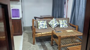 A room with a wooden sofa, a small wooden table, a purple object on a cabinet, and a patterned rug. - Kay's Place Cultural Apartment Zanzibar Gallery (Zanzibar)