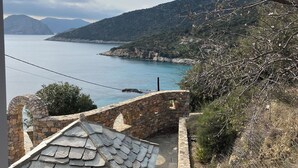 Un bâtiment en pierre doté d’un toit en pente, d’un mur en pierre et offrant une vue sur un paysage côtier avec des montagnes et une étendue d’eau.