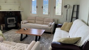 Un salon comprenant un canapé, une table basse, une cheminée et une vue sur l’extérieur grâce à de grandes fenêtres.