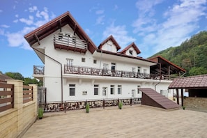 A multi-story building with balconies, a covered area, and a paved courtyard.