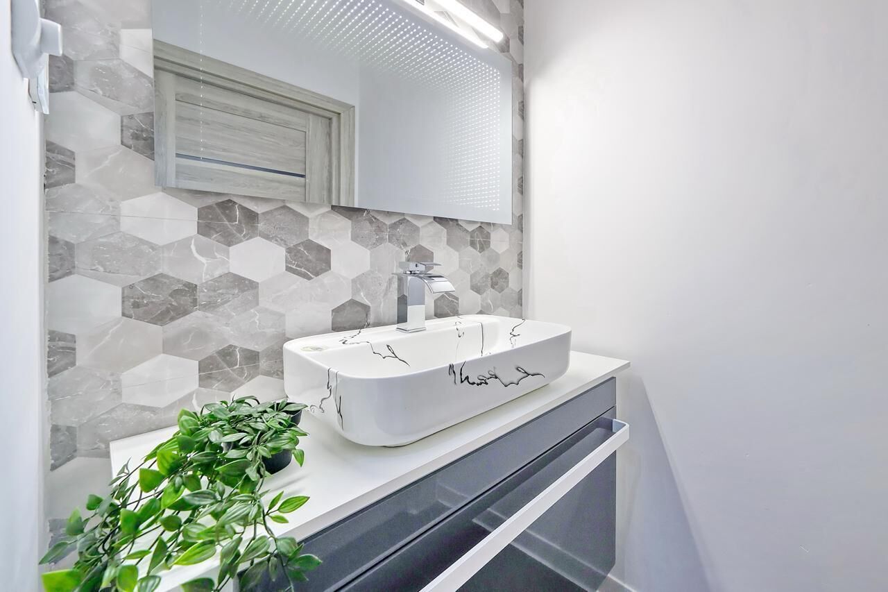 A modern bathroom with a white sink, a mirror, and a hexagonal tile backsplash.