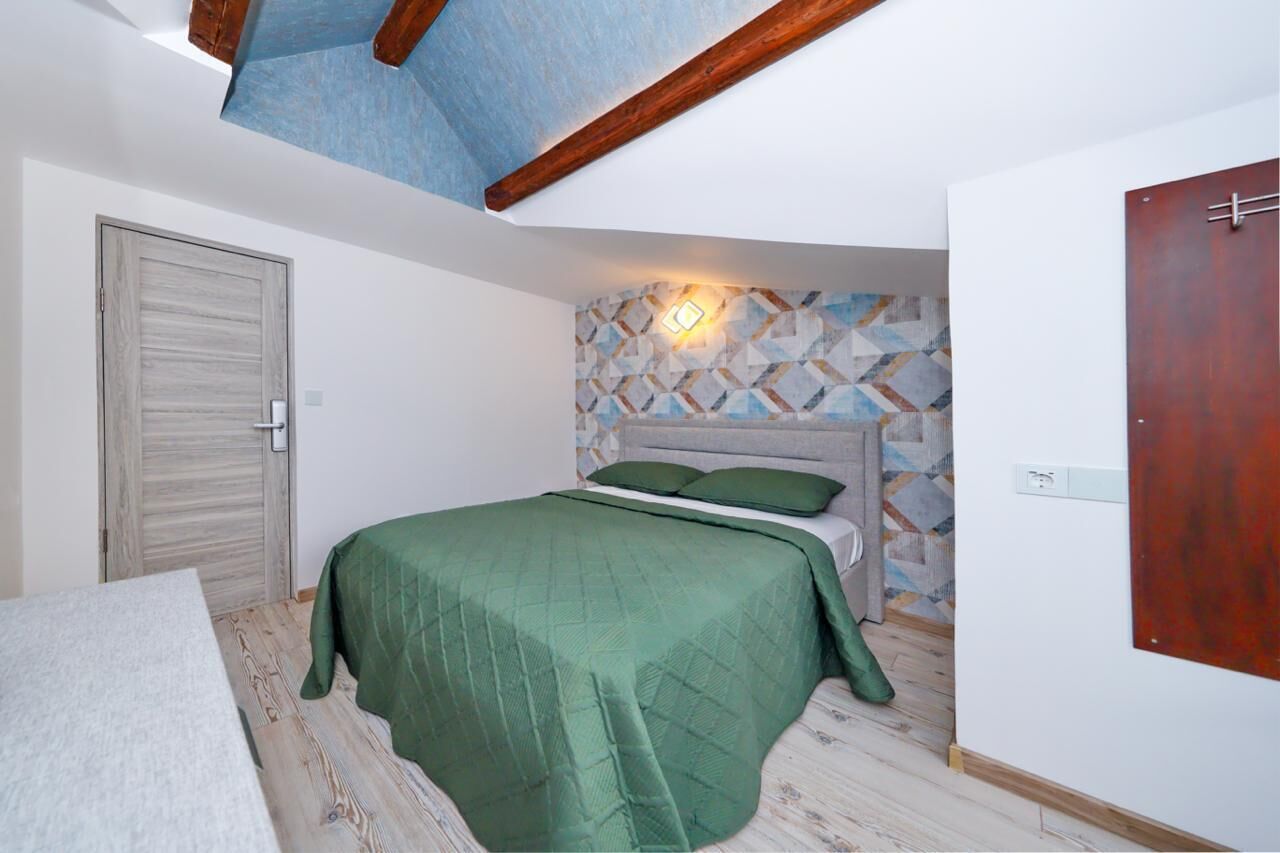 Un dormitorio con cama, puerta de madera, pared con diseño y techo con vigas a la vista.