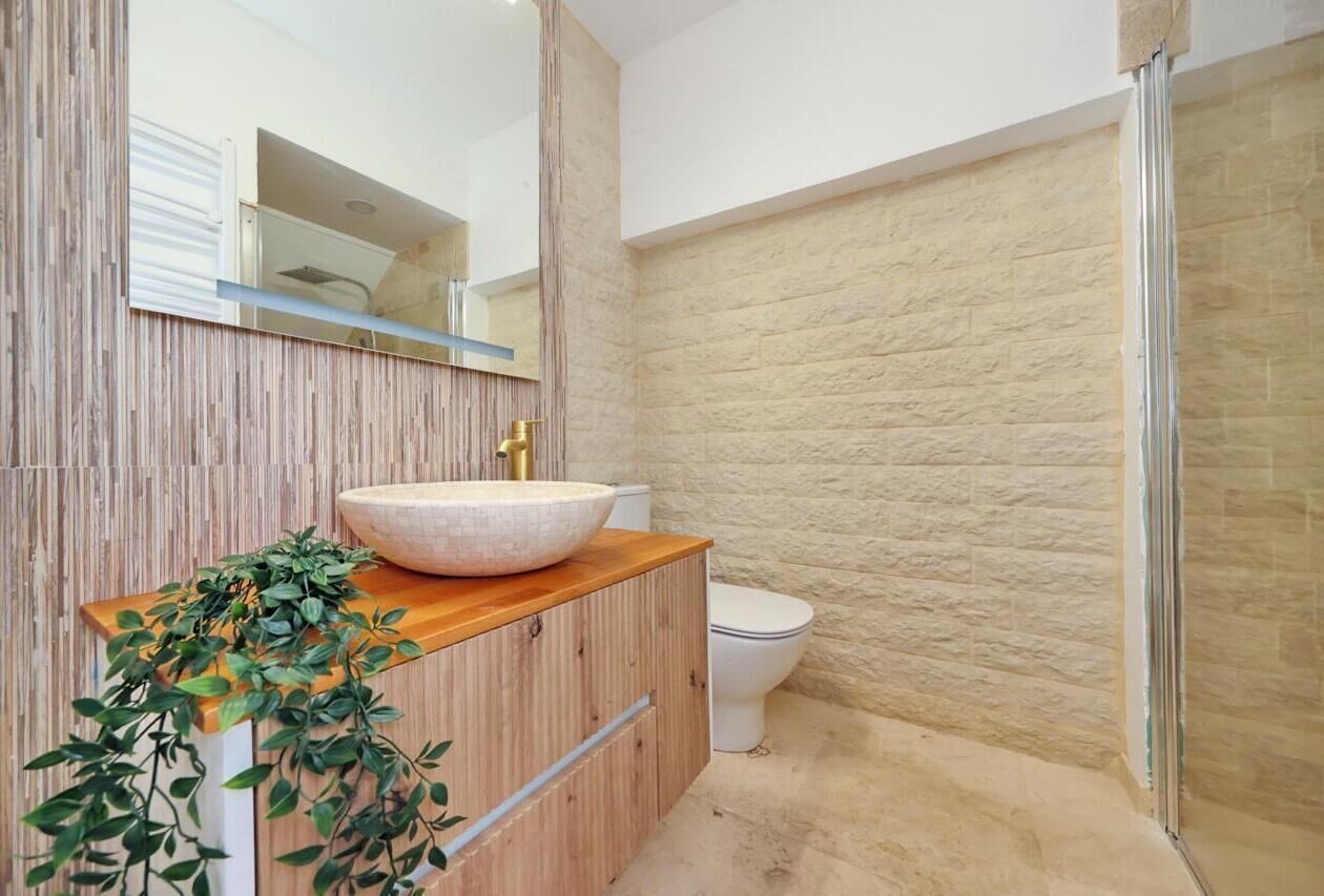 A bathroom with a wooden vanity, a large mirror, a white sink, and a toilet.