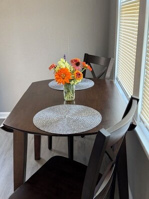 A dining table with two placemats, a vase with flowers, and chairs.