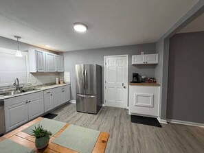 Une cuisine moderne avec des meubles blancs, des appareils en acier inoxydable et une table à manger en bois agrémentée d’une plante.