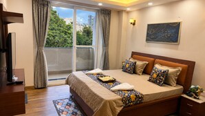 A hotel room with a bed, a TV, a desk, a window with curtains, and a painting on the wall. - Sukhvan Residency (Gurugram)