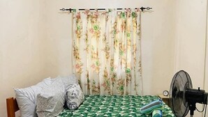 Ein Zimmer mit einem Bett, einem Ventilator und einem Vorhang mit Blumenmuster.