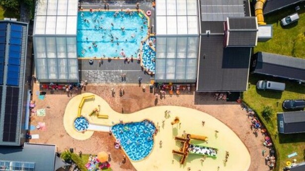 Vue aérienne d’un espace piscine comprenant une plage de sable, un toboggan aquatique et une aire de jeux pour enfants.