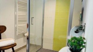 Een moderne badkamer met een glazen douchecabine, een wit toilet, een klein houten stoeltje en een kamerplant.
