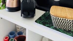 Een keukenwerkblad met een koffiezetapparaat, een waterkoker en een zwart apparaat, mogelijk een rijstkoker of slowcooker, op een wit schap.