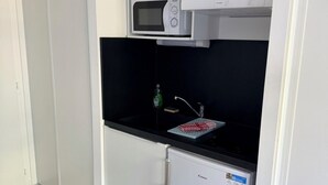 Een compacte kitchenette met een magnetron, een kleine koelkast en een spoelbak met een afwasschaal.