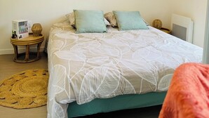 Een slaapkamer met een bed, twee kussens, een klein rond tafeltje met een boek en een geweven mat.