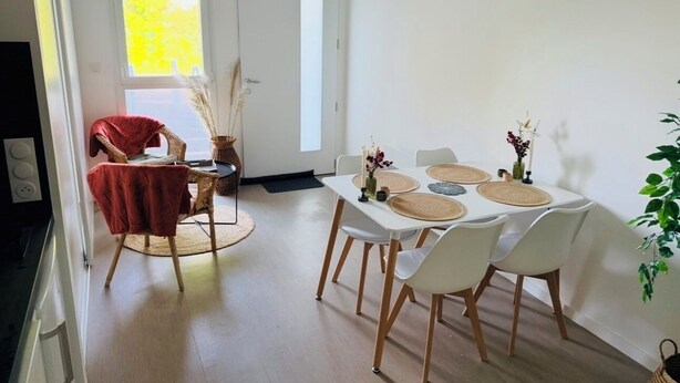 Een eethoek met een tafel voor vier personen, omringd door witte, rode en rieten stoelen.