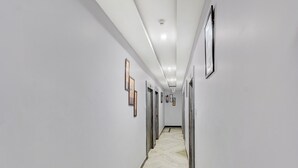 A hallway with white walls, framed pictures, and a marble floor. - Deluxeamba Palace (Prayagraj)